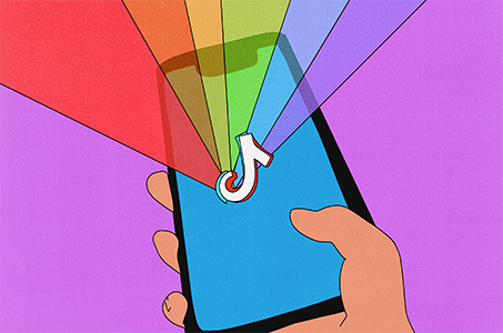 An illustration shows a hand holding a cellphone with the colors of the LGBTQ flag in the background.