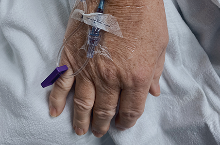 Closeup of a patient's arm with an IV inserted. The elderly woman is being treated for COVID.