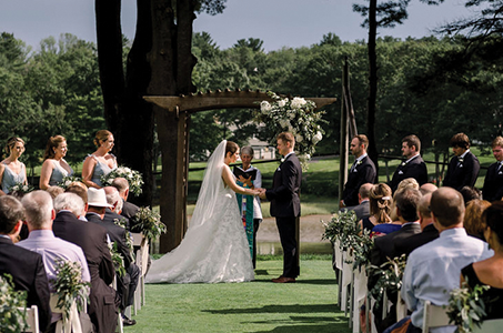 A couple getting married, holding hands as they take their vows in front of a crowd of seated guests