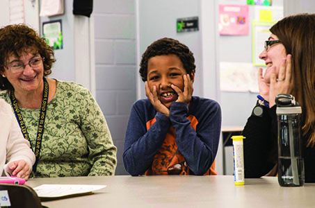 A smiling young boy sitting at a table between two women teachers at the New England Center for Children.