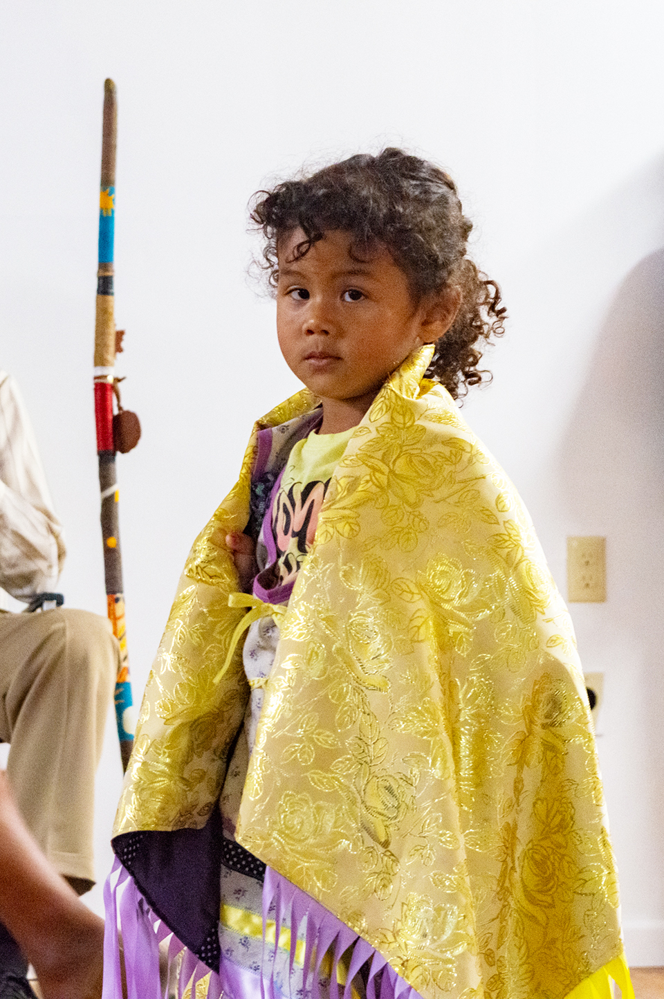 Greendeer's youngest daughter looks into the camera in a vibrant yellow and gold shawl.