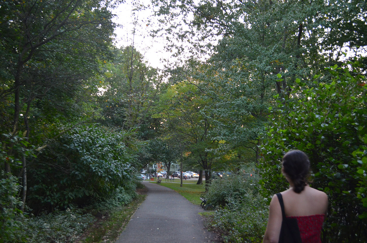 Isabel Janeff, a brunette wearing a terracotta tube top, is seen from the back walking between two tall, lush bushes