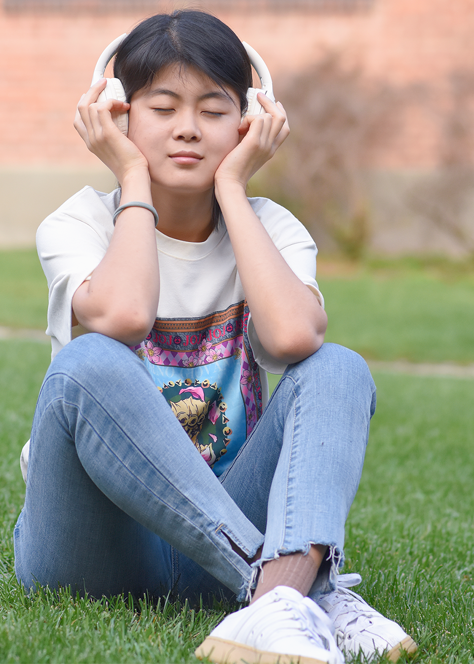 Emily Jing, sitting on the grass and listening to music wearing headphones with her eyes closed