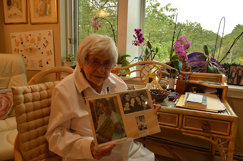 Esther Adler wearing a white shirt sits at her desk in her home in Canton holding a photograph of her family