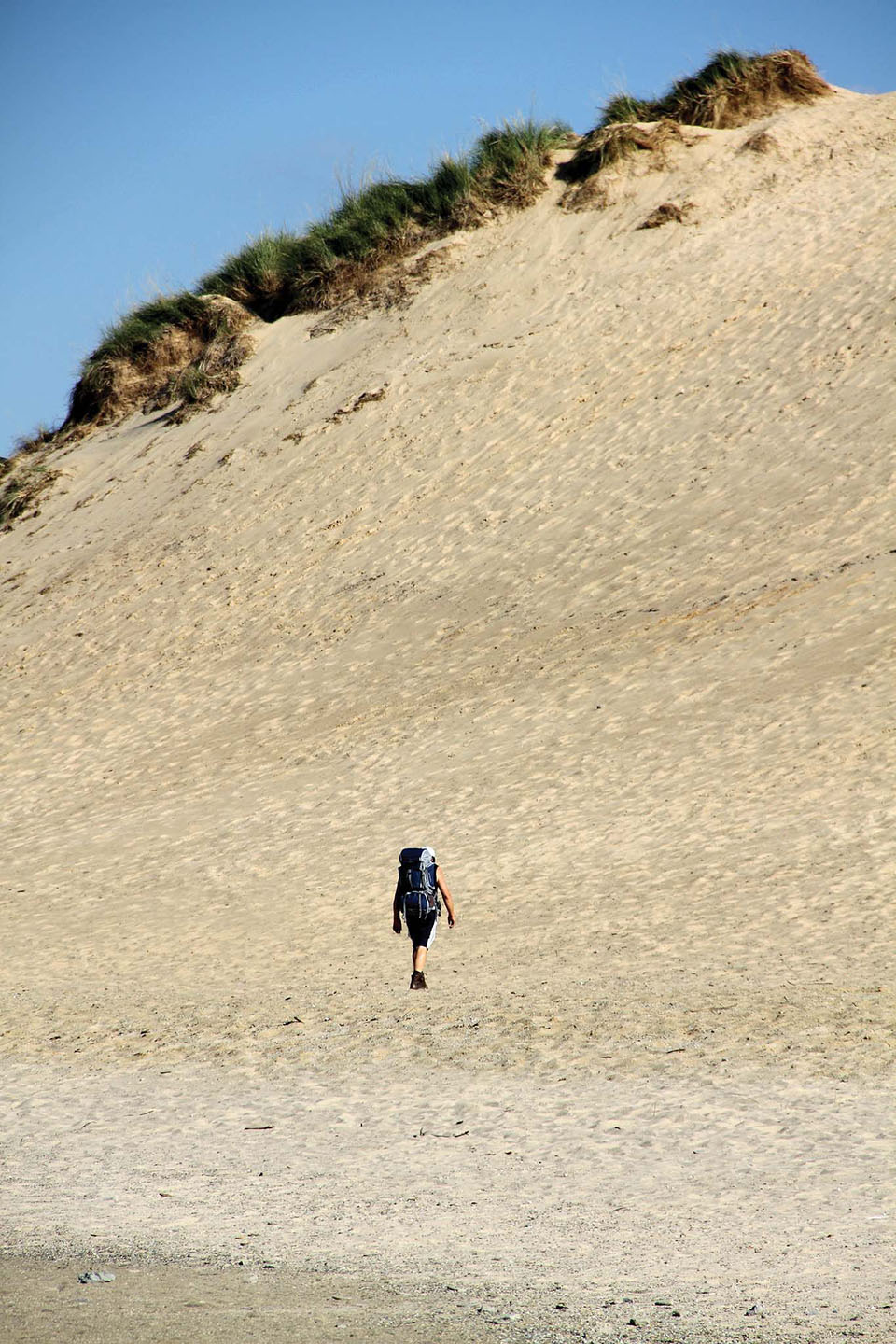 A man in a black backpacking bag walks through the sand on Mount Baldy in Pines, Indiana.