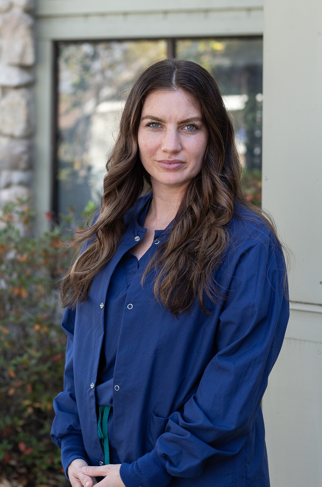 pictured: Amanda Mckee standing looking at the camera. She has brown hair and blue scrubs.