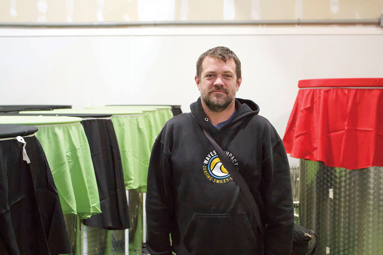 Dylan L'Abbe-Lindquist stands in the middle of the fermentation room, surrounded by tanks with different colored sheets on top